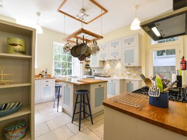 A kitchen with blue stools island pot rack and cabinets with tiled backsplash at Woodlands in Dartmouth