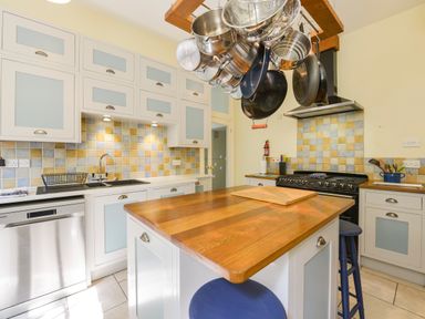 A kitchen with white cabinets and a wooden countertop island with hanging pots at Woodlands in Dartmouth