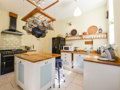 A kitchen with a center island with hanging pots a stove a black refrigerator and wooden countertops at Woodlands in Dartmouth