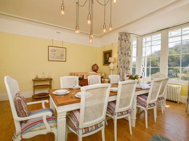A dining room with a large wooden table and white chairs with striped cushions at Woodlands in Dartmouth