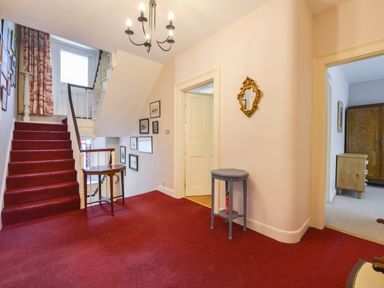 A stairway with red carpet leading to upper floor with framed pictures on walls and a small table in a hallway at Woodlands in Dartmouth