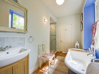 A bathroom with a white sink cabinet and mirror a chair a bathtub and a shower at Woodlands in Dartmouth