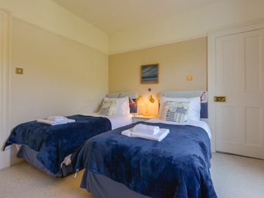 A bedroom with two single beds with navy blankets and bedside table with lamp at Woodlands Dartmouth