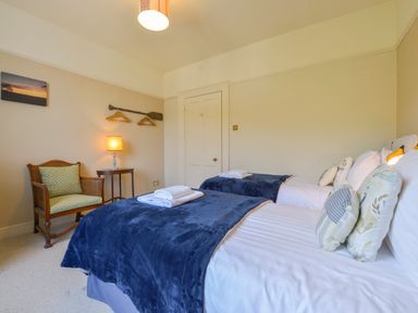 A bedroom with two single beds lined with blue blankets and pillows a wooden chair with a green cushion a small table with a lamp and hangers on the wall at Woodlands in Dartmouth