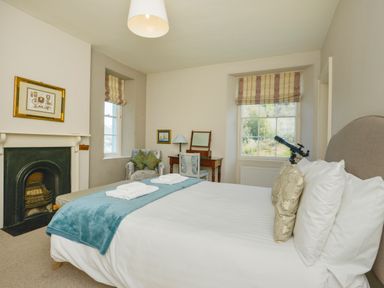 A bedroom with a bed a fireplace an armchair a desk with a lamp and a telescope at Woodlands in Dartmouth