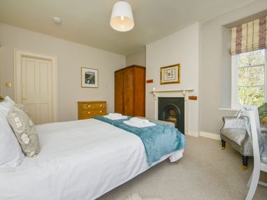 A bedroom with a double bed blue throw towels on bed wooden wardrobe wooden chest of drawers framed pictures fireplace and a window at Woodlands in Dartmouth