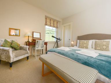 A bedroom with a bed a striped bench an armchair a desk with mirror a window and a telescope at Woodlands Dartmouth