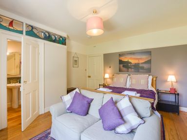 A bedroom with a bed, sofa with pillows, bedside tables with lamps, and a partially open door revealing a bathroom at Woodlands in Dartmouth