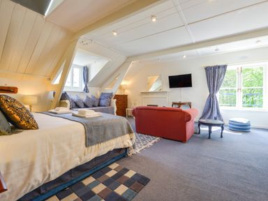 A bedroom with bed sofa armchair television and window with blue curtains at Woodlands in Dartmouth