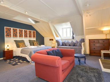 A bedroom with a double bed a red sofa a blue side table a cushioned bench under a window and a wooden dresser at Woodlands in Dartmouth