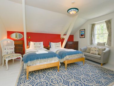 A bedroom with two single beds a patterned rug a sofa and a window at Woodlands in Dartmouth