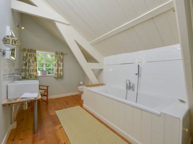 A bathroom with a bathtub a sink a toilet wooden floor and a window with curtains at Woodlands in Dartmouth