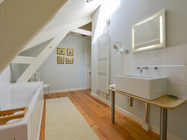 A bathroom with a bathtub a sink a mirror a radiator wooden floor and framed pictures on the wall at Woodlands in Dartmouth