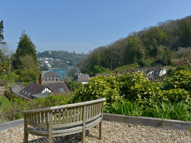 A wooden bench on a gravel area overlooking houses bushes trees a river and hills at Woodlands in Dartmouth