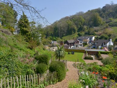 A garden with pathways flowers and shrubs overlooking houses and a wooded hill at Woodlands Dartmouth