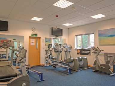 A gym room with treadmills rowing machines stationary bikes and televisions at Fixit Cottage in Kingsbridge