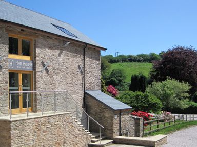 Stone building with Hen House fitness health and beauty sign surrounded by green trees and flowers at Fixit Cottage in Kingsbridge