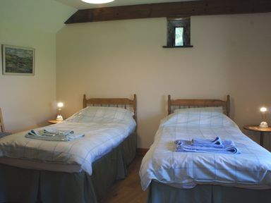 A bedroom with two single beds and bedside tables with lamps at The Clock House in Ivybridge