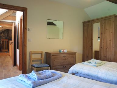 A bedroom with two single beds with folded towels on them a wooden wardrobe chest of drawers and a chair at The Clock House in Ivybridge