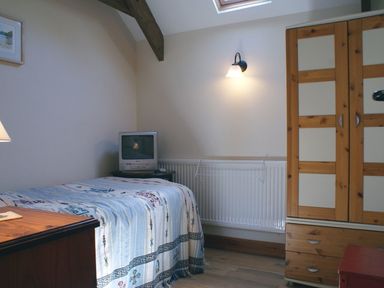 A bedroom with a bed a small television a wooden wardrobe and a wall light at The Clock House in Ivybridge