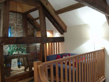 An attic room with wooden beams a blue sofa with red cushions and a wooden railing at The Clock House in Ivybridge
