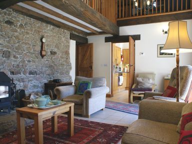 A living room with armchairs a wooden coffee table and a stone wall at The Clock House in Ivybridge