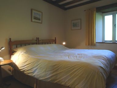 A bedroom with a double bed a bedside table with a lamp framed pictures on the walls and a window with curtains at The Clock House in Ivybridge