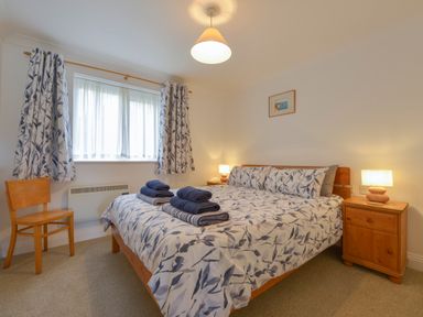 A bedroom with a double bed with folded towels bedside tables with lamps and a wooden chair at 5 Burgh Island Causeway in Bigbury-on-Sea