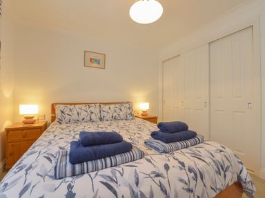 A bedroom with a double bed having patterned bedding and folded towels on top between two wooden bedside tables with lamps at 5 Burgh Island Causeway Bigbury-on-Sea
