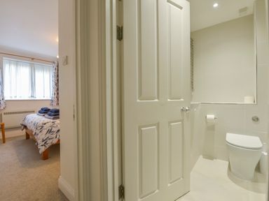 A bedroom with a bed and folded towels and an adjacent bathroom with a toilet at 5 Burgh Island Causeway in Bigbury-on-Sea