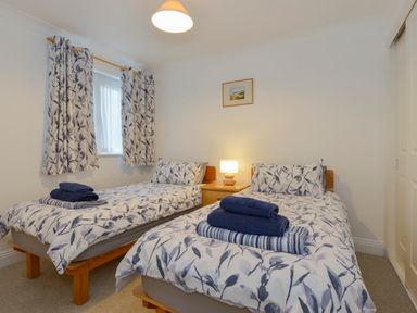 A bedroom with two single beds side by side with matching leaf-patterned bedding and curtains at 5 Burgh Island Causeway in Bigbury-on-Sea