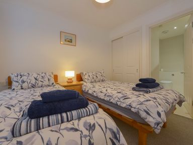 A bedroom with two single beds with patterned bedding a bedside table with a lamp and an open door leading to a bathroom at 5 Burgh Island Causeway in Bigbury-on-Sea