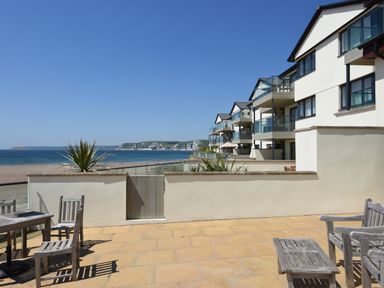 A patio with wooden chairs and tables overlooking the beach and sea at 5 Burgh Island Causeway in Bigbury-on-Sea