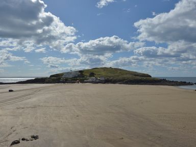 A sandy beach with a hill and buildings in the background under a partly cloudy sky at 5 Burgh Island Causeway in Bigbury-on-Sea
