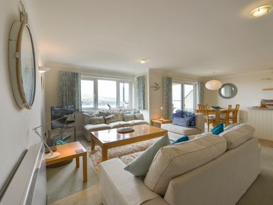 A living room with sofas, a coffee table, a flat screen TV, and a dining table in the background at 13 Burgh Island Causeway in Bigbury-on-Sea