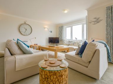 A living room with two sofas a wooden coffee table a large wall clock and a television at 13 Burgh Island Causeway Bigbury-on-Sea