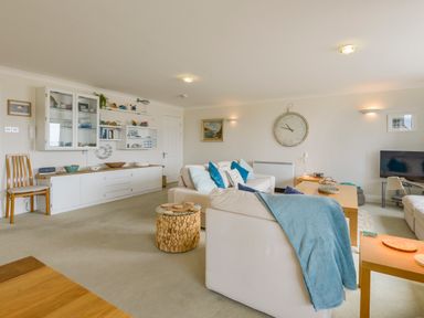 A living room with white sofas blue pillows a wooden clock on the wall and shelving at 13 Burgh Island Causeway in Bigbury-on-Sea
