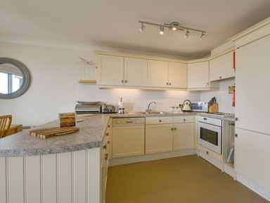 A kitchen with cream cabinets a gray countertop a dishwasher an oven a microwave and a round mirror on the wall at 13 Burgh Island Causeway in Bigbury-on-Sea