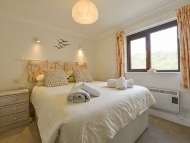 A bedroom with a double bed pillows bedside table window and rolled towels at 13 Burgh Island Causeway in Bigbury-on-Sea