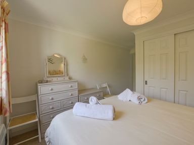 A bedroom with a bed with rolled towels on it two white chairs a dresser with a mirror and a closet with sliding doors at 13 Burgh Island Causeway in Bigbury-on-Sea