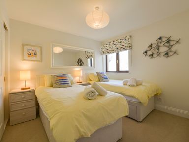 A bedroom with two single beds with yellow bedding a window with a patterned blind and fish-themed decor at 13 Burgh Island Causeway in Bigbury-on-Sea