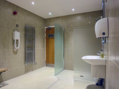 A bathroom with a glass shower door a towel radiator a wall-mounted hairdryer and a sink with soap at 13 Burgh Island Causeway in Bigbury-on-Sea