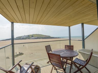 A balcony with wooden table and chairs overlooking a sandy beach and island at 13 Burgh Island Causeway Bigbury-on-Sea