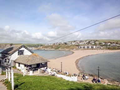 A beach with houses on the shore and people sitting outside near a white building at 13 Burgh Island Causeway in Bigbury-on-Sea