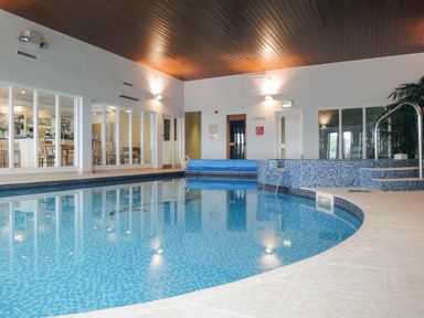 An indoor swimming pool with blue mosaic tiles and a seating area behind glass walls at 13 Burgh Island Causeway in Bigbury-on-Sea