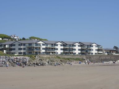 A beach with people and a large apartment building behind rocks at 27 Burgh Island Causeway in Bigbury-on-Sea