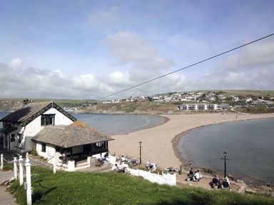 A seaside cafe with people sitting outside near a curved sandy beach and sea at 27 Burgh Island Causeway in Bigbury-on-Sea