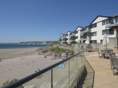 A beach with people and a patio with tables and umbrellas next to a row of buildings at 27 Burgh Island Causeway in Bigbury-on-Sea