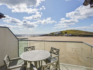 An outdoor balcony with a round table and four chairs overlooking a sandy beach and a distant hill at 24 Burgh Island Causeway in Bigbury-on-Sea