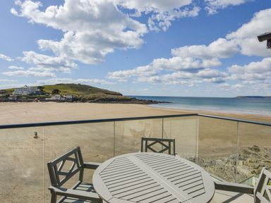 A balcony with a round table and chairs overlooking a sandy beach and the sea at 24 Burgh Island Causeway in Bigbury-on-Sea